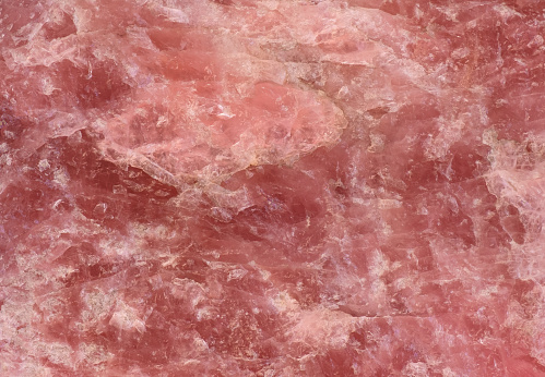 A rose colored quartz stone texture / structure, part of a larger rose quartz rock with a natural shape and a rough surface. The closeup is well usable for backgrounds and textures.