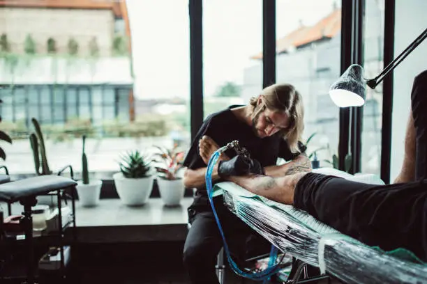Artist making tattoo on customer's leg in studio