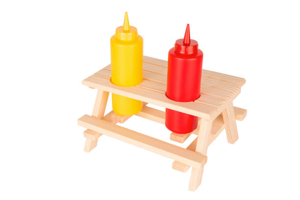 Tomato ketchup and mustard bottles on tiny picnic table. Isolated on white background.