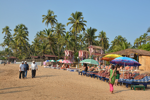 Goa, India-November 9,2016: Tourists relax on sun loungers under umbrellas at Anjuna beach near beach cafes