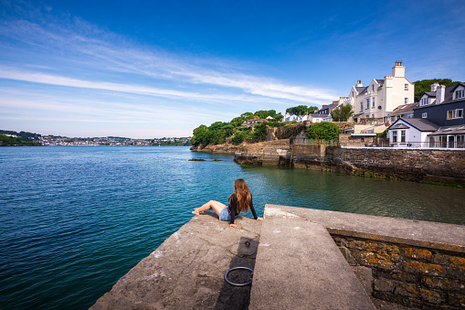 A female Asian tourist in her 40s is soaking up the Summer Irish sun along the coastline of Kinsale in Country Cork. She's enjoying the affluent neighborhood of Summer Cove.