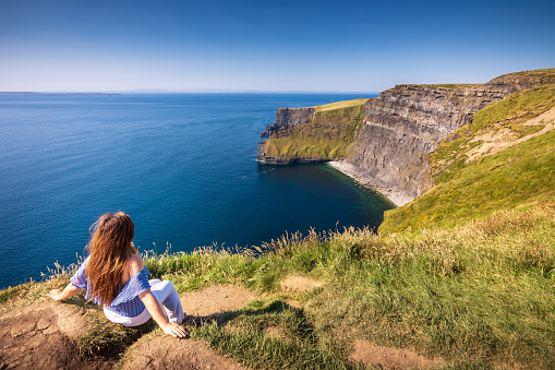 An Asian woman in her 40's is traveling alone, and enjoying the spectacular view of the Cliffs of Moher, which are 200m high cliffs located at the southwestern edge of the Burren region in County Clare, Ireland.