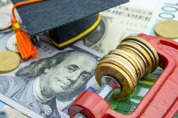 Financial austerity / budget control concept : Coins held by a c clamp on US dollar notes and graduation cap, depicts the economic policies a government implements to reduce debt on education sector. Financial austerity / budget control concept : Coins held by a c clamp on US dollar notes and graduation cap, depicts the economic policies a government implements to reduce debt on education sector. budget cut stock pictures, royalty-free photos & images