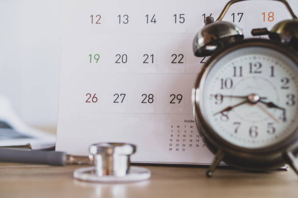 стол кабинета врача с календарным будильником и стетоскопом - проверка время стоковые фото и изображения