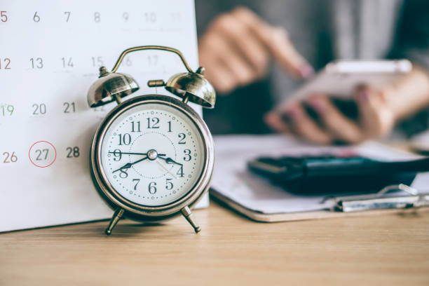 calendario y reloj despertador con desenfoque de negocio mujer mano calculando - colección fotografías e imágenes de stock