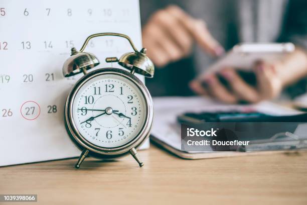 Due Date Calendar And Alarm Clock With Blur Business Woman Hand Calculating Stock Photo - Download Image Now