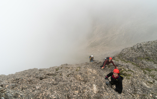 three young attractive male and female mountain climbers on a steep and exposed Via Ferrata in Alta Badia in the South Tyrol in the Italian Dolomites