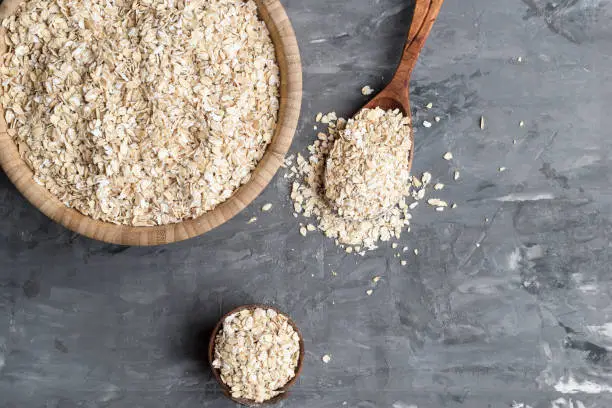 Rolled oats in wooden bowl, spoon, on a concrete background, top view. Copy space