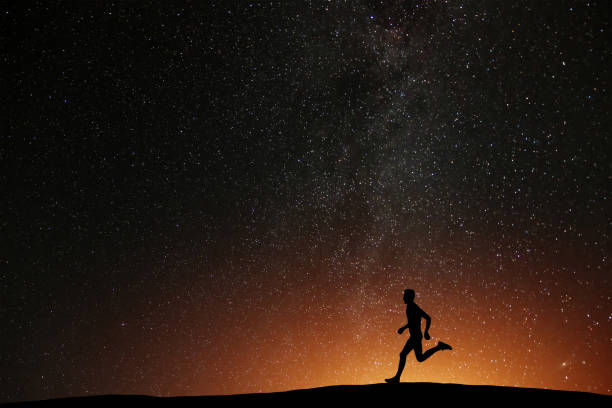 runner athlete running on the hill with beautiful starry night background. silhouette of man jogging workout in dark time, wellness concept. - night running imagens e fotografias de stock