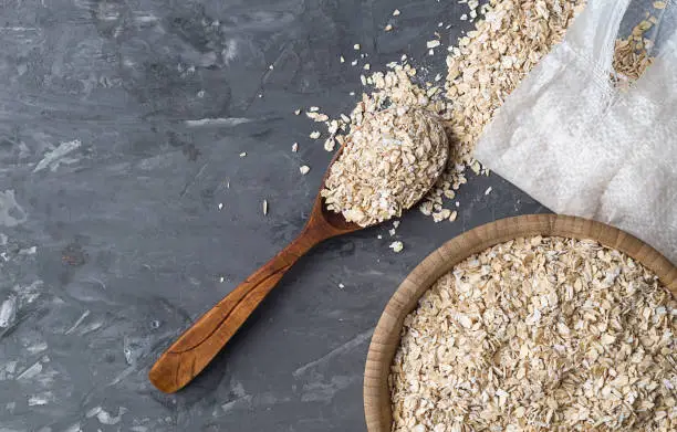 Rolled oats or oat flakes in wooden bowl, spoon, white bagon a concrete background, top view. Copy space