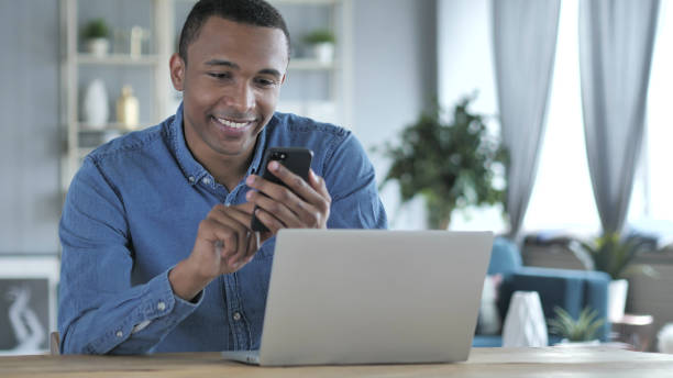istock Young African Man Using Smartphone and Laptop at Work 1039473734