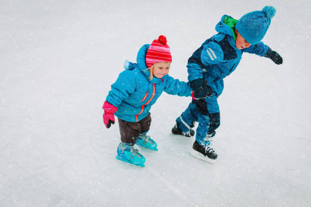 little boy and girl skating together, kids winter sport stock photo