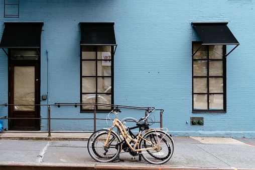 New York City, USA - June 22, 2018:  Bicycles parked besides old apartment building with brick facade painted in blue at Greenwich Village
