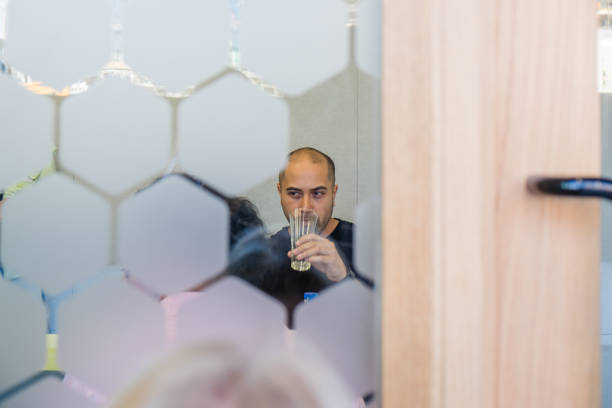 Looking through frosted glass into an interview room: man with facial stubble is drinking glass of water Looking through frosted glass into an interview room: man of mixed maori/caucasian ethnicity with facial stubble is drinking glass of water frosted glass door office stock pictures, royalty-free photos & images
