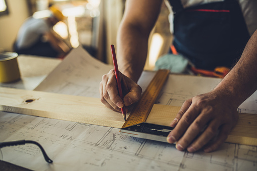 Close up of unrecognizable carpenter making measurements and drawing on a plank.