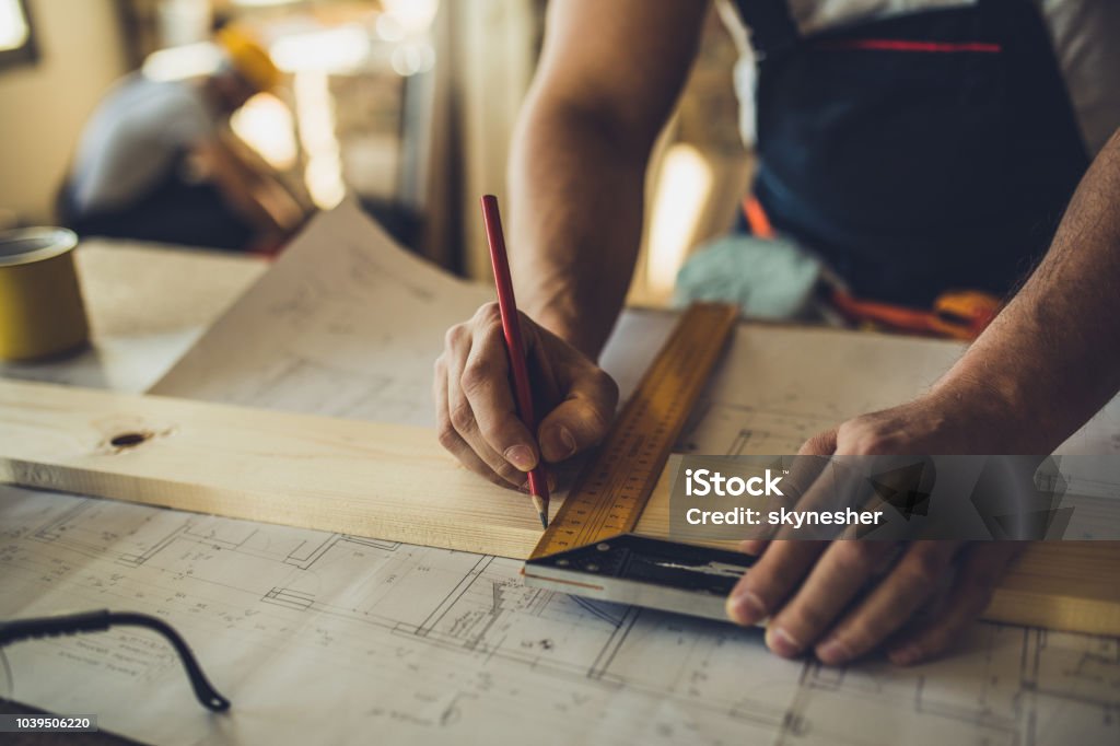 Close up of unrecognizable worker drawing on wood plank. Close up of unrecognizable carpenter making measurements and drawing on a plank. Carpenter Stock Photo