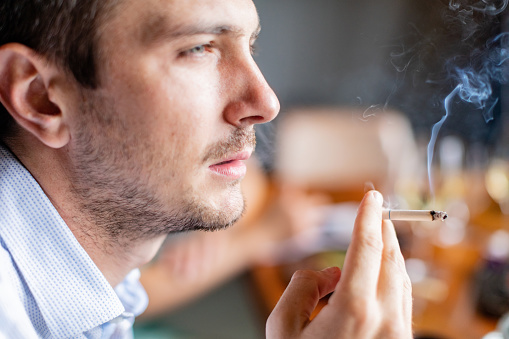 Young businessman smoking cigarette after lunch in sushi bar