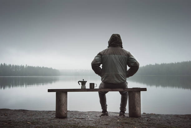 istock A man is sitting on a bench and looking at the lake. Back view. Also a coffee maker and a mug on the bench. 1039546168