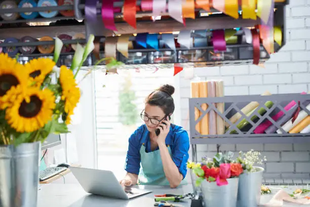 Portrait of young female businesswoman managing flower shop and speaking by phone, copy space