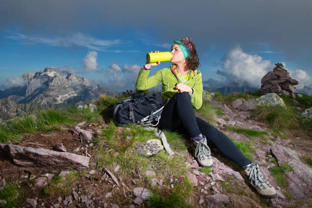 uma garota desportiva bebe na garrafa de água, depois de ter conquistado o topo de uma montanha - conquered - fotografias e filmes do acervo