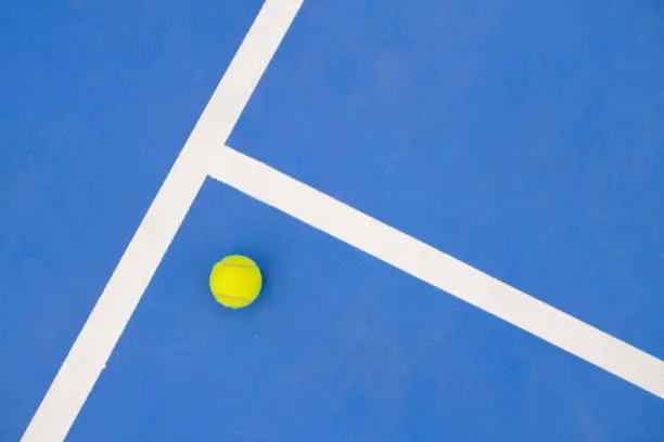 Graphic sports background of yellow tennis ball laying on blue floor in court, copy space