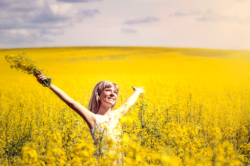 Woman with long hair standing on yellow rapeseed meadow with raised hands. Concept of freedom and happiness