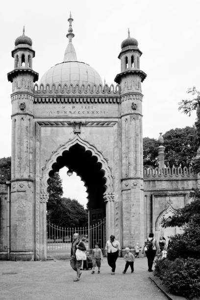 Brighton Pavilion's familiar copper domed arched entrance to the grounds with intricately decorated stone towers surrounding it. There is a group of tourists walking past the arch.