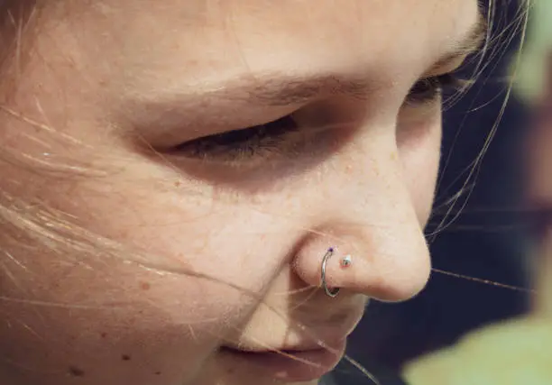 A young woman with a fresh nose piercing looking off camera