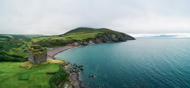 Aerial panorama of the Minard Castle situated on the rocky beach of the Dingle Peninsula with views across the Irish Sea in Kerry county, Ireland.