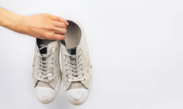 istock White dirty sneaker shoes with hand holding on white background 1039590894