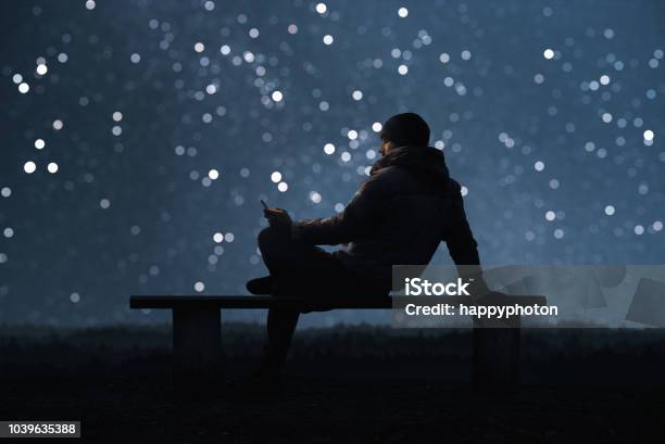 Ein Mann Sitzt Auf Einer Bank Und Per Smartphone Sternenhimmel Bokeh Im Hintergrund Stockfoto und mehr Bilder von Himmel