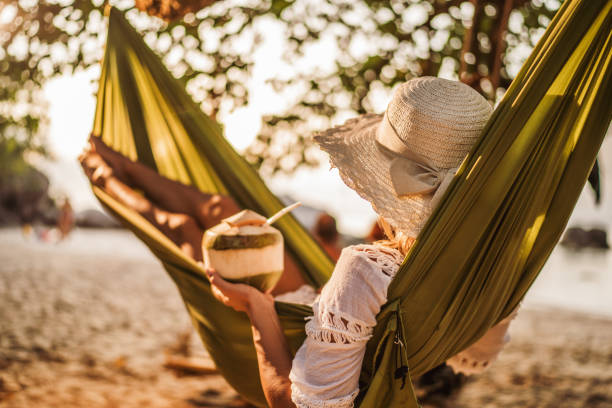 donna con bevanda al cocco rilassante sull'amaca in spiaggia. - hammock beach vacations tropical climate foto e immagini stock