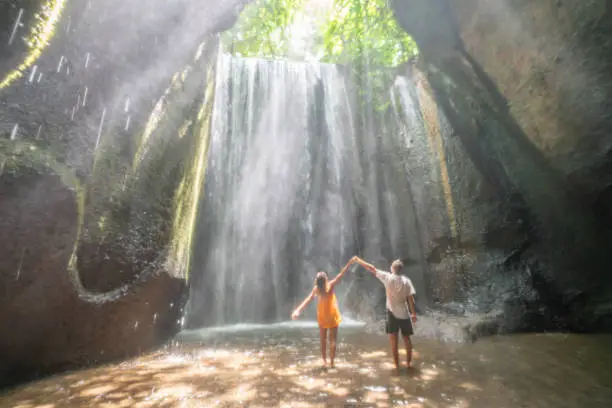 Photo of Young couple standing in tropical rainforest cave looking up at the magnificent sunbeam coming from the rocks above. People travel wonderlust nature concept