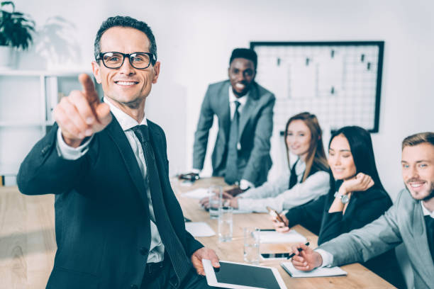 istock handsome businessman pointing at camera with multicultural partners sitting in conference hall blurred on background 1039666528