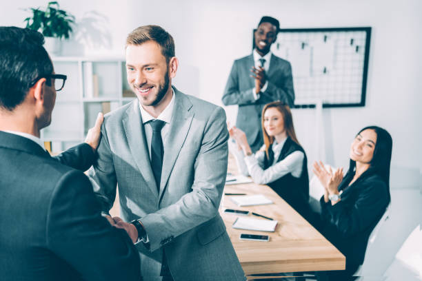 istock businessmen shaking hands in conference hall with multicultural partners sitting at table 1039668612
