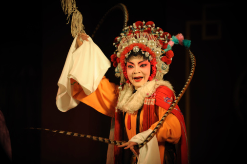 Female performer of Georgian folk dances dressed in Georgian traditional costume. She dances on a stage bathed in light.