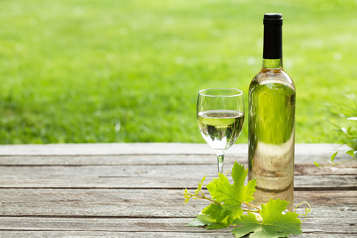White wine bottle and glass on wooden table. Outdoor still life. With space for your text