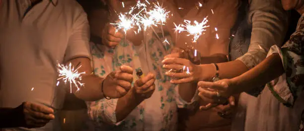 Photo of panoramic view of group of friends mixed ages celebrate together in the night with sparkles file light. new year eve or birthday or Christmas event to live friendship and family with happiness and spent nice time