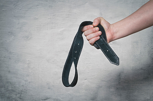 Hand holds leather belt for punishment. Family violence concept.