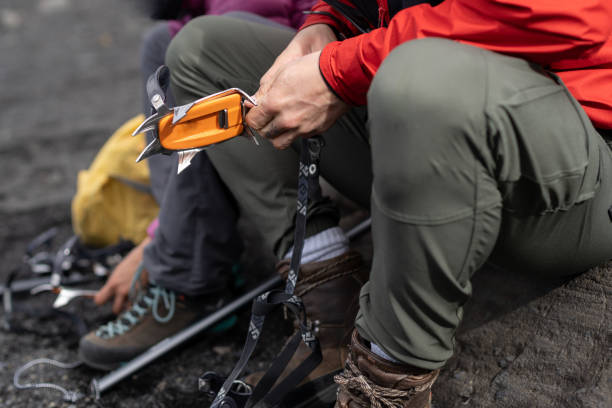 Profile side view cropped photo of alpinist masculine man in red bright waterproof jacket and green pants hold anti-slip hiking crampons device, prepare to dangerous training climb track in mountain vista lateral de perfil recortado foto de hombre masculino alpinista en rojo brillante chaqueta y pantalones verdes mantenga antideslizante senderismo dispositivo de crampones, se preparan para formación peligrosa pista de subida en la montaña