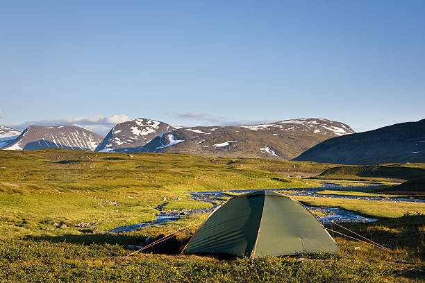 First sun beams appearing over the tall mountains. The soft sunlight reaches the tent, from which the shot was taken. A new day is waking up to life. Camping in the wilderness.