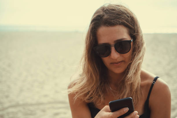 istock Woman on her 30s checking the phone against a blurred beach background with Selective focus on the hand holding the phone 1039714272