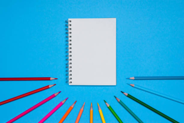 istock Top view on a note book with blank and color pencils on a blue background 1039715046