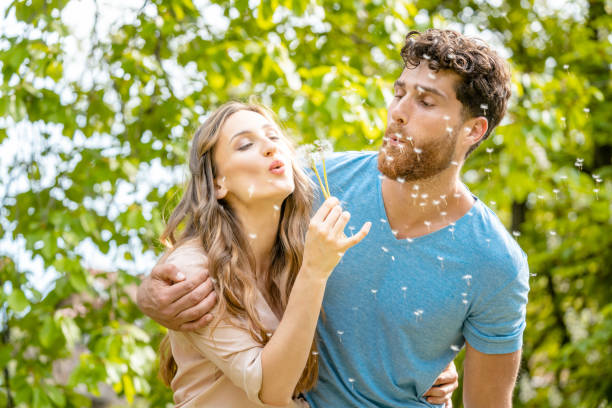 Young couple daydreaming about their future blowing dandelion seeds Young couple daydreaming about their future blowing dandelion seeds being visibly happy man flower stock pictures, royalty-free photos & images