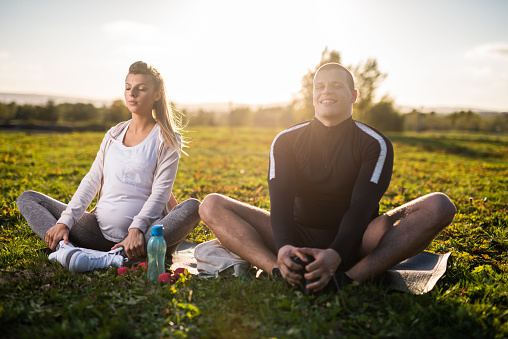 Young couple meditating in nature at sunset.