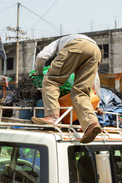 Unidentified Ghanaian man climbs on the car at the Kumasi market. KUMASI, GHANA - JAN 15, 2017: Unidentified Ghanaian man climbs on the car at the Kumasi market. 11313 stock pictures, royalty-free photos & images