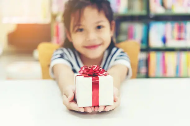 Gift box for kids girl.  White box with red bow in the girl hands for give a gift in the library