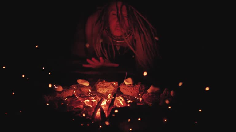 Scary witch does voodoo black magic ritual near the fire at night. Halloween horror