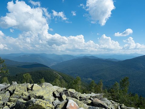 Carpathians mountains, west Ukraine. Pile of grey natural stones. White clouds flowing in blue sky. Mountain ranges with green woods. Ukrainian nature landscape in august. Blurred background