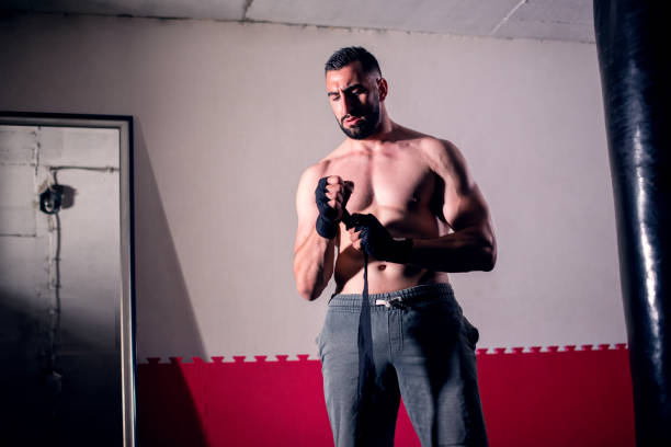 Female boxer is wrapping hands with red boxing wraps. Isolated on black background with copy space. Strong hand and ready for fight, active exercise and sparring. Close up. Women self defense.